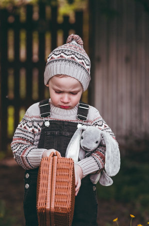 A little boy of 4 years old outdoors with a suitcase and a stuffed rabbit goes on a journey. A beautiful portrait of a child playing on the street.の写真素材