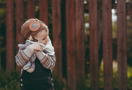 A little boy of 4 years old in an aviator hat and stylish clothes plays outdoors in spring. Portrait of a child with a soft toy in his hands. happy childhood.の写真素材