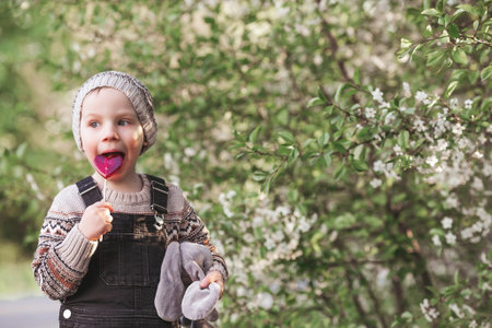 A little boy of 4 years old in stylish clothes outdoors with a lollipop in the shape of a heart. A...