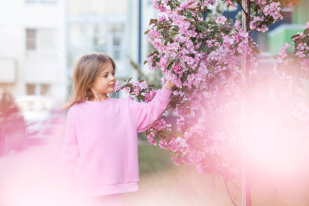 spring flowering. Portrait of a beautiful little girl 4 years old in a pink blouse in nature against a background of pink flowering apple trees. Childhood. The baby is posing.の写真素材