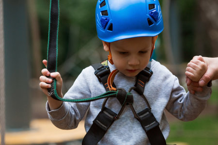 Summer. A small child climbs in a rope park on a rope bridge. A boy is having fun in an Adventure Park. A male baby on a climbing frame. Compliance with safety techniques.の写真素材
