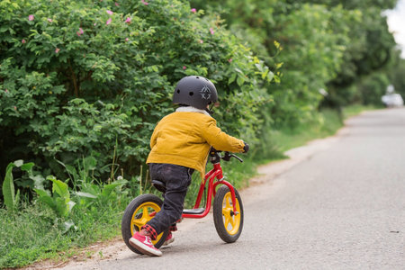 A cheerful little boy rides a running bike in a helmet outdoors. A happy child is engaged in an active sport. protection. Life insurance and child safety.の写真素材