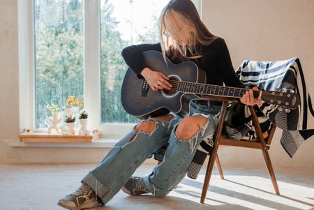 Music and hobbies. A talented young musician girl sits alone and composes songs on the guitar. The girl plays a calm melody on a musical instrument.の写真素材