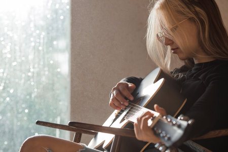 Music and hobbies. A talented young musician girl sits alone and composes songs on the guitar. The girl plays a calm melody on a musical instrument.の写真素材