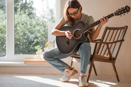 Music and hobbies. A talented young female musician sits alone and composes songs on the guitar. The...
