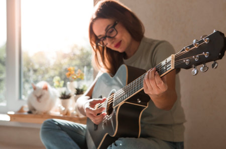 Music and hobbies. A talented young female musician sits alone and composes songs on the guitar. The lady plays a calm melody on a musical instrument.の写真素材