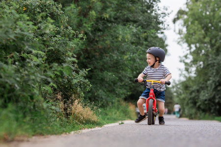 A cheerful little boy rides a running bike in a helmet outdoors. A happy child is engaged in an active sport. protection. Life insurance and child safety.の写真素材
