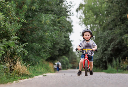 A cheerful little boy rides a running bike in a helmet outdoors. A happy child is engaged in an active sport. protection. Life insurance and child safety.の写真素材