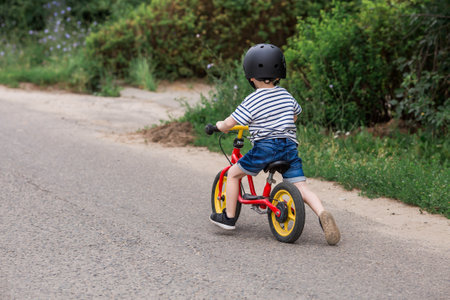 A cheerful little boy rides a running bike in a helmet outdoors. A happy child is engaged in an active sport. protection. Life insurance and child safety.の写真素材
