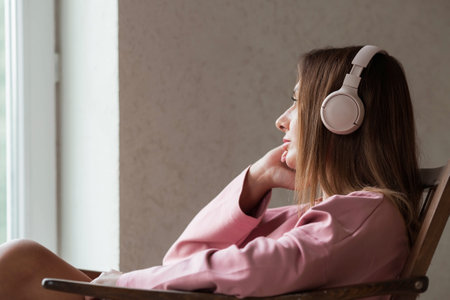 A young beautiful woman listening to music with headphones with her eyes closed sitting on a retro wooden chair.. Peace, harmony, relaxation and relaxation.の写真素材