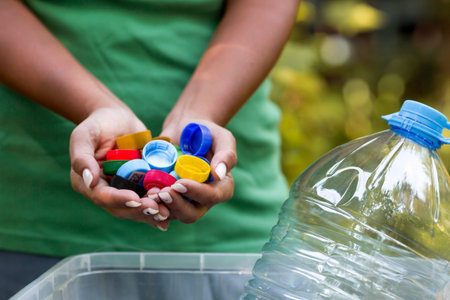 A woman's hands hold the lids of plastic bottles for recycling and environmental conservation,...