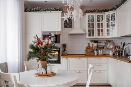 A spruce bouquet with red berries, toys, cotton on a white kitchen table. Christmas decorations in the interior. The concept of preparation for the New Year's holiday 2024.の写真素材
