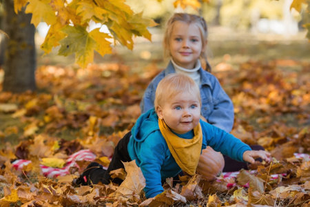 Portrait of a little boy 9 months old and a girl 4 years old outdoors. Happy children in the autumn park with pumpkins. Happy childhood and fatherhood.の写真素材