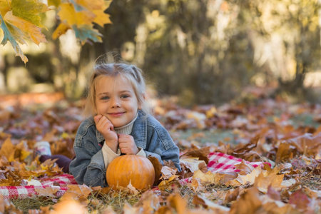 Portrait of a little girl 4 years old outdoors. A happy child in an autumn park with pumpkins. Happy...