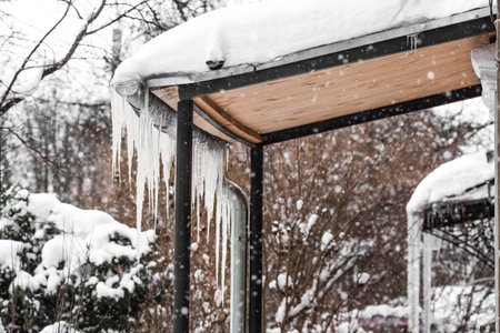 Carefully. Danger. Beautiful sharp icicles and snow hang from the eaves of the roof. Transparent icicles slide across the roof.の写真素材