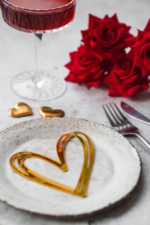 The banner. Table setting. Stylish ceramic plate, glass of red wine, red roses, fork and golden hearts on a concrete background. The concept of celebrating Valentine's Day for cafes and restaurants.の写真素材