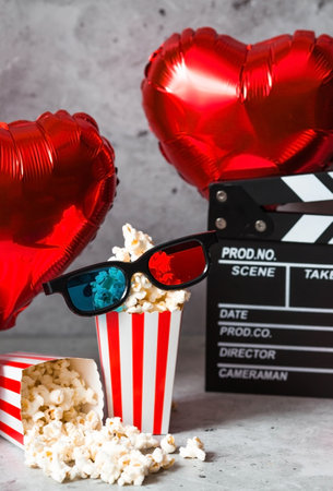 A banner for the film industry. A romantic movie date. A movie camera, 3D glasses, popcorn and foil balloons in the shape of hearts on a concrete gray background. The film will premiere on Valentine's Day.の写真素材