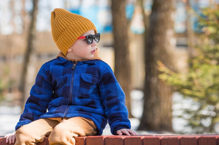 A cheerful little boy walks outside in the spring. She will rub the baby in a fashionable plaid shirt, yellow hat and sunglasses in the sunlight.の写真素材