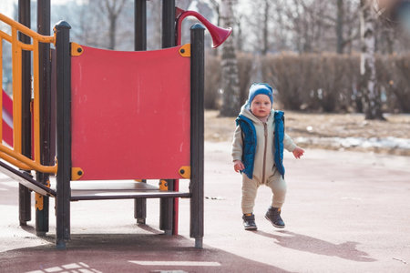 A handsome, cheerful little boy of two years old walks on the street in the spring. A kid in overalls and a blue vest walks through the park. The concept of parenthood, childhood and family.の写真素材