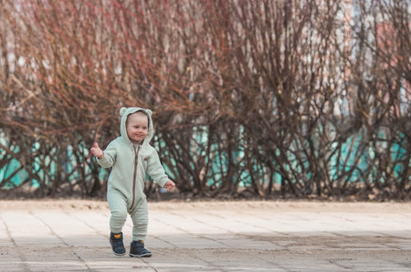 A handsome, cheerful little boy of two years old walks on the street in the spring. A kid in overalls and a blue vest walks through the park. The concept of parenthood, childhood and family.の写真素材
