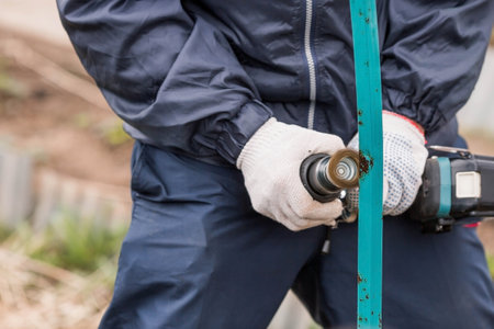 A man works with an electric grinder to clean rust from metal iron structures. Rust removal using an electric iron brush. Hands in work gloves are holding a power tool.の写真素材