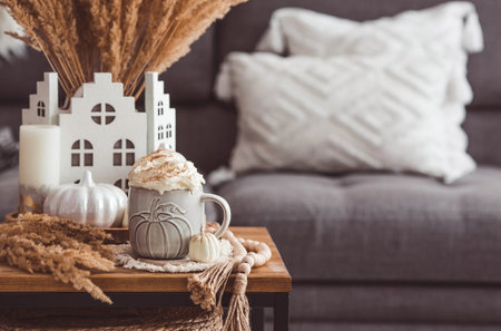 A seasonal drink. Delicious pumpkin latte with whipped cream and cinnamon in a mug on a wooden table in the living room interior.Autumn decor in the house. Scandinavian style.の写真素材