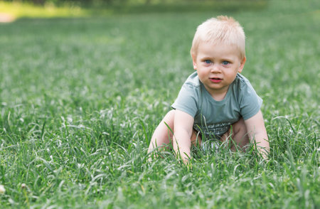 Portrait of a little boy 1.5 years old in the fresh air. A happy child in a summer park on a green lawn. The guy is wearing a green T-shirt. Happy childhood and fatherhood.の写真素材