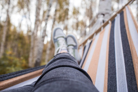 Outdoor recreation. Women's legs, shod in sneakers, in a hammock in the autumn forest. The concept...