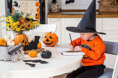 A little boy of 5 years old paints a Halloween picture at a table in the kitchen interior. Festive decor for decorating a cozy home.の写真素材