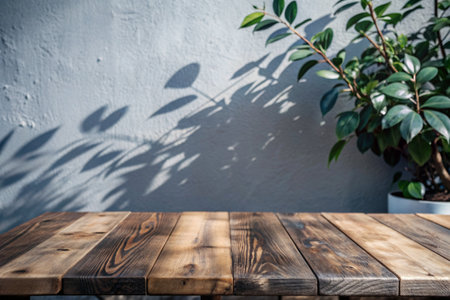 An empty old wooden countertop against a gray wall with sunlight and shadows from the leaves of trees. Background for the presentation and advertising of goods.の素材