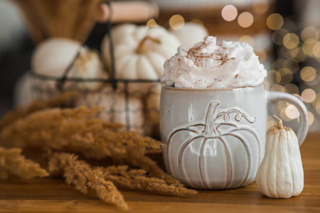 Delicious pumpkin latte with whipped cream and cinnamon in a mug on the table in the living room interior. Autumn decor in the house. Scandinavian style.の写真素材