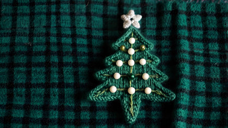 A Christmas card. Knitted green Christmas tree on the background of a knitted plaid. Knitting, crafts, handmade jewelry.の素材