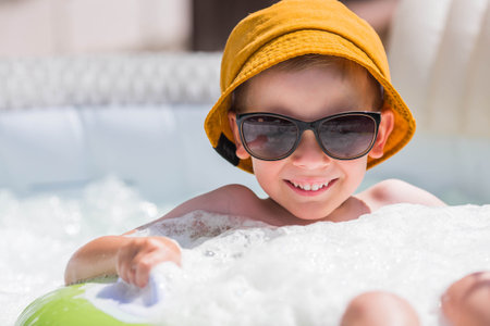 It's a hot day. A cute boy in sunglasses and a panama hat swims on a circle in a foam pool. The concept of summer holidays with children.の写真素材