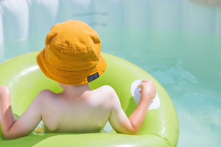It's a hot day. A cute boy in sunglasses and a panama hat swims on a circle in a foam pool. The concept of summer holidays with children.の写真素材