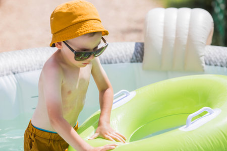 It's a hot day. A boy in sunglasses and a hat swims on a circle in a foam pool. The concept of summer holidays with children.の写真素材