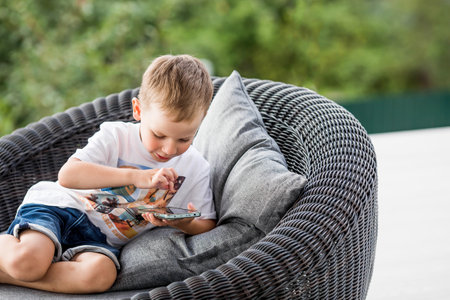 A 5-year-old little boy with a smartphone in his hands on the veranda. The child is playing on the phone.の写真素材