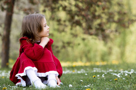 Spring blooming. Portrait of a beautiful 5-year-old girl in a red dress in a blooming garden in nature. Childhood.の写真素材