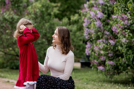 Family and motherhood. Spring blooming. Portrait of a pretty 30-year-old mother and her daughter in a blooming lilac garden in nature.の写真素材