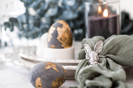 The banner. Table setting. A plate with a rabbit and a napkin, Easter eggs with gilding and a branch...
