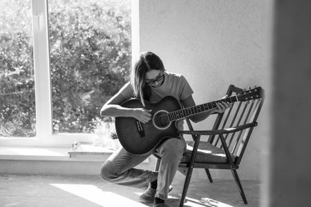 A talented young female musician sits alone and composes songs on the guitar. She plays a calm melody on a musical instrument.Music and hobbies.の写真素材