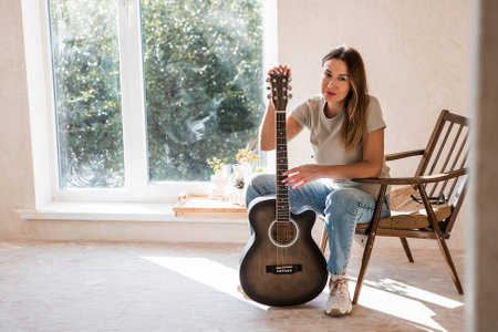 A talented young female musician sits alone and composes songs on the guitar. She plays a calm melody on a musical instrument.Music and hobbies.の写真素材