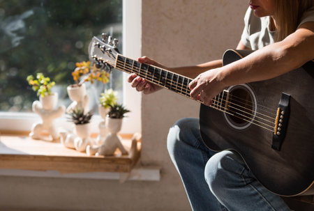 A talented young female musician sits alone and composes songs on the guitar. She plays a calm melody on a musical instrument.Music and hobbies.の写真素材