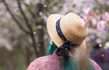 Portrait. A girl in a straw hat with green hair in a Japanese garden against a background of cherry blossoms. Sakura blossoms in the garden.の写真素材