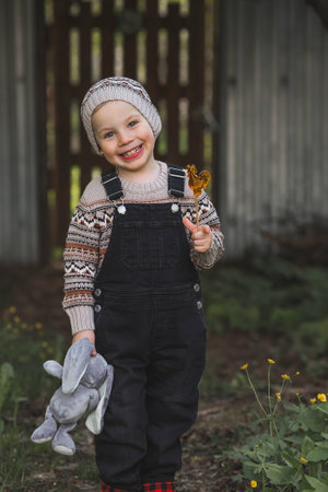 Childhood. A little boy on the street with a stuffed rabbit and a lollipop. Beautiful portrait of a child playing outside.の写真素材