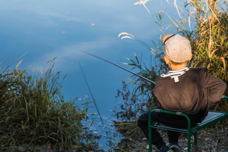 A little boy fishing on a warm autumn day on a pond.の写真素材