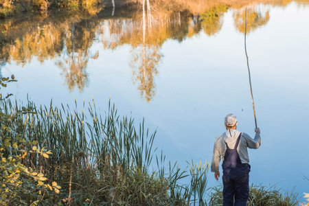 A man fishing on a warm autumn day on a pond.