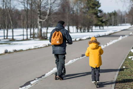 A little boy in bright yellow clothes and his dad rides. A happy child and father are walking outside in early spring. Happy childhood and family.の写真素材