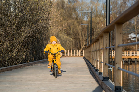 A boy in bright yellow clothes rides a bike. A happy child plays outside in early spring. Happy childhood.の写真素材