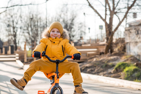 A cute boy in bright yellow clothes rides a bike. A happy child plays outside in early spring. Happy childhood.の写真素材