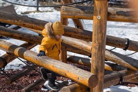 A boy in bright yellow clothes is playing on the playground. A climber climbs a structure. A beautiful portrait of a child playing outside in early spring. Happy childhood.の写真素材